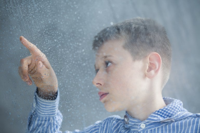 Autistischer Junge zählt Regentropfen an Fensterscheibe
