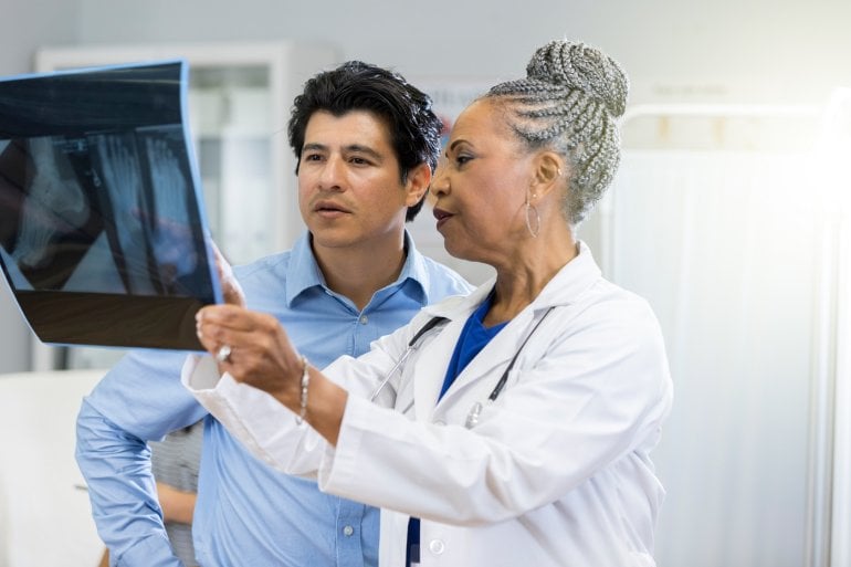 Ärztin zeigt Mann Knochenbruch auf Röntgenbild