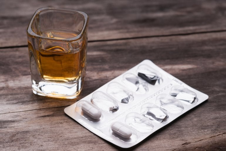 Ein Glas mit Alkohol und eine Packung Antibiotika-Tabletten