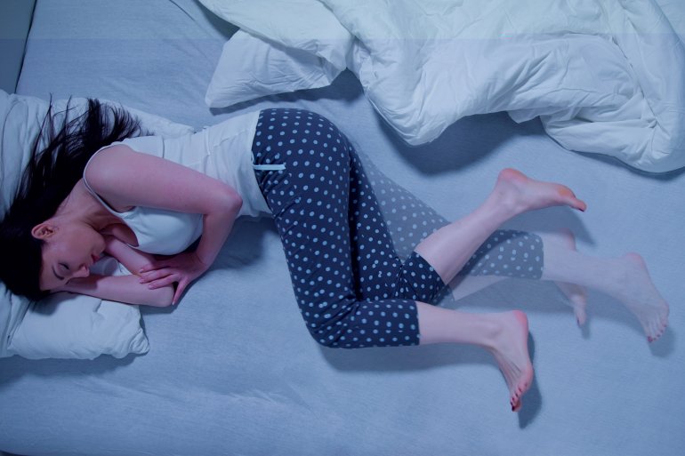 Frau liegt nachts mit unruhigen Beinen (Restless-Legs-Syndrom) im Bett