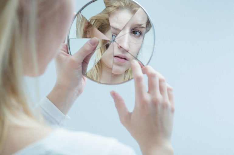 Psychopathische Frau betrachtet sich in zerbrochenem Spiegel