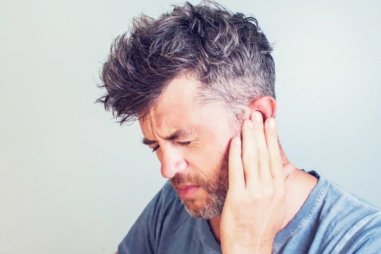Mann mit Tinnitus greift an sein Ohr