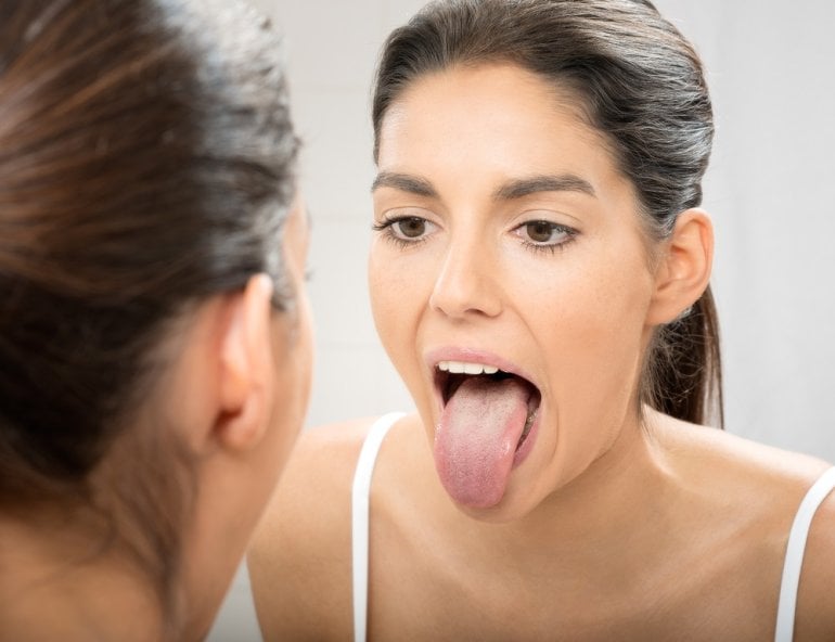 Frau betrachtet geschwollene Zunge im Spiegel